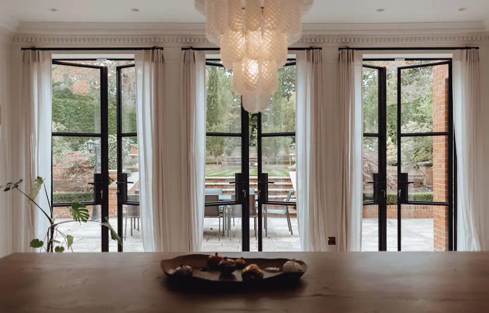 Black steel and glass French doors opening from a dining room onto a garden